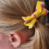 Barrette jaune à fleurs roses en forme de nœud dans les cheveux d'une petite fille.